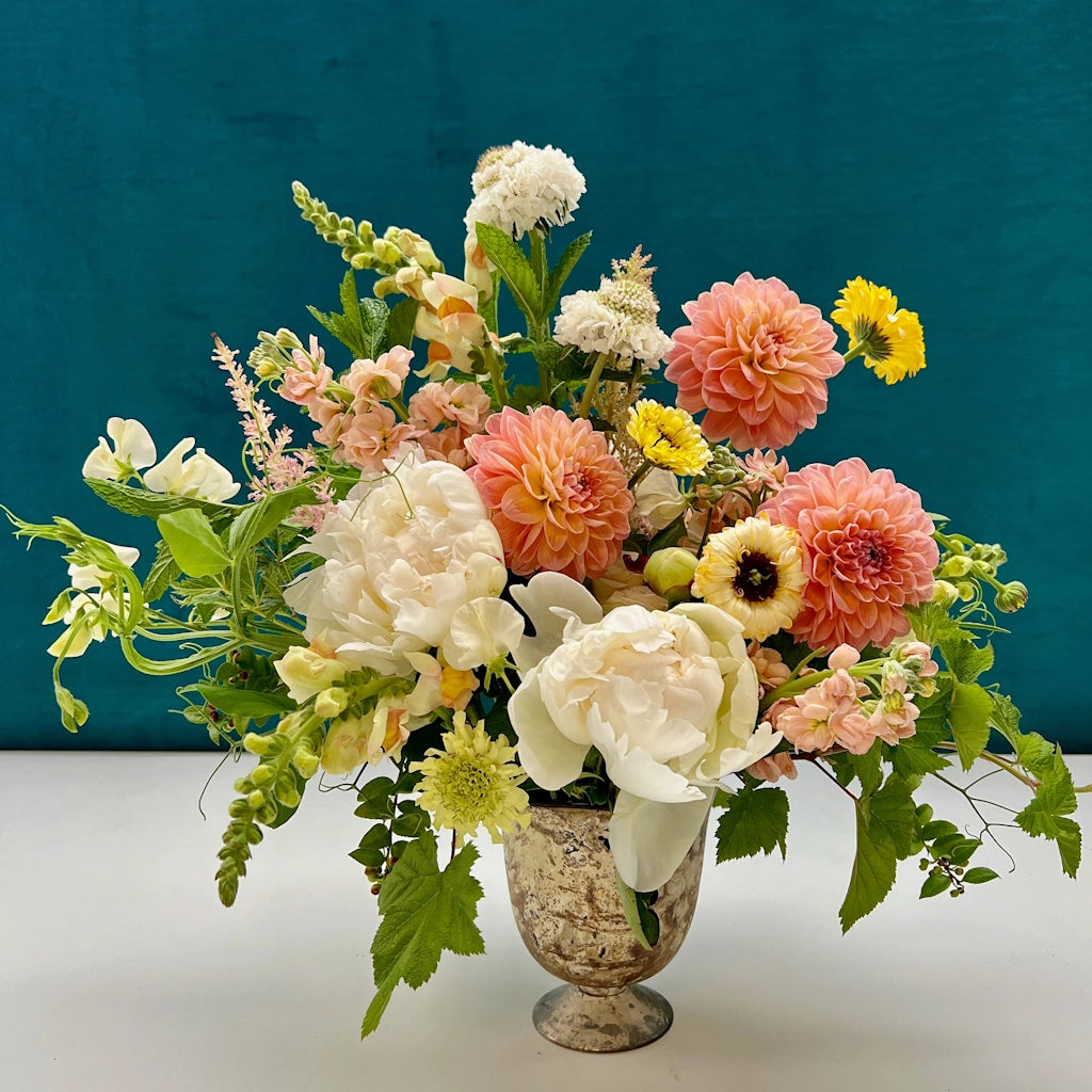Flower arrangement with a soft collection of peach and cream toned blooms designed in a small vase.