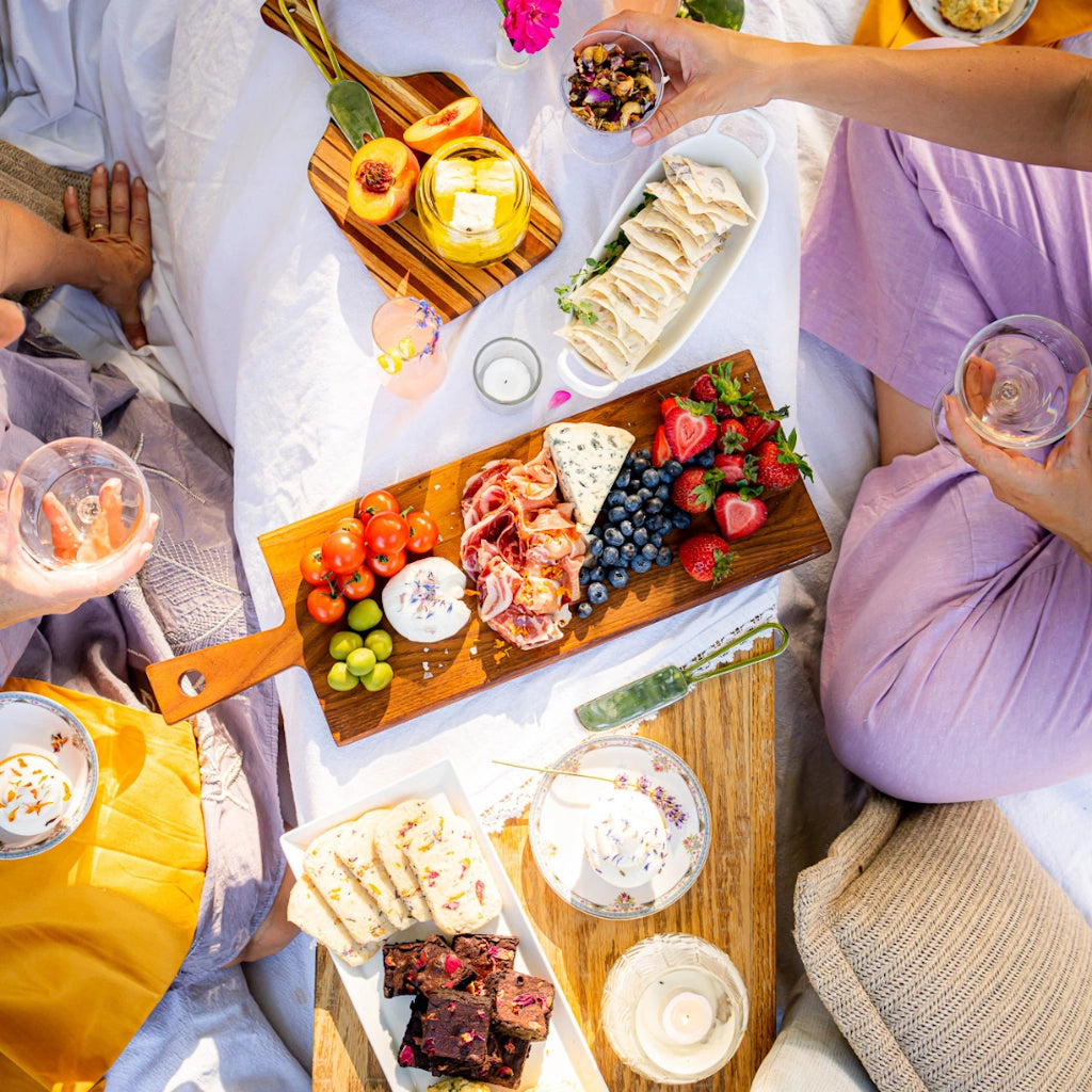 People enjoying a picnic with charcuterie boards, fruits, and drinks on a blanket.