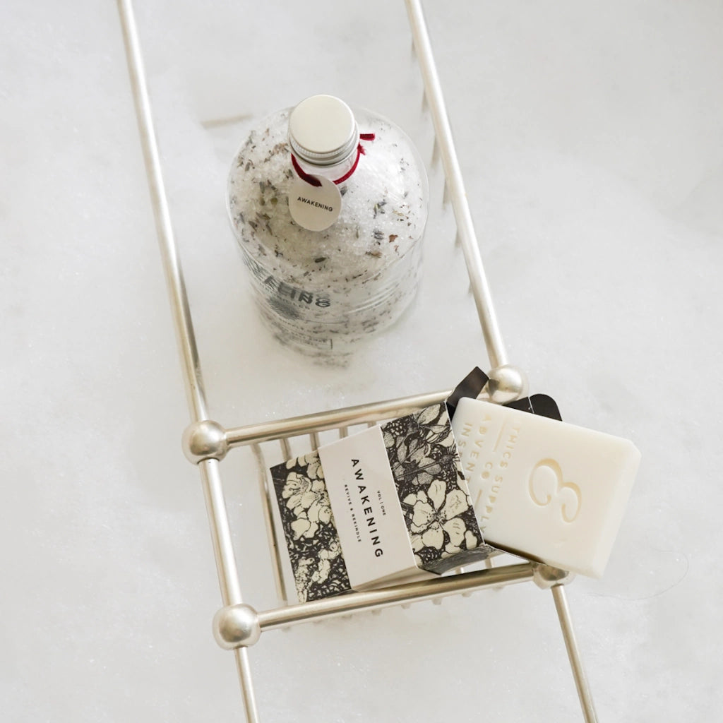 Bath Salt Bottle, soap, and book on a small metal shelf against a white background