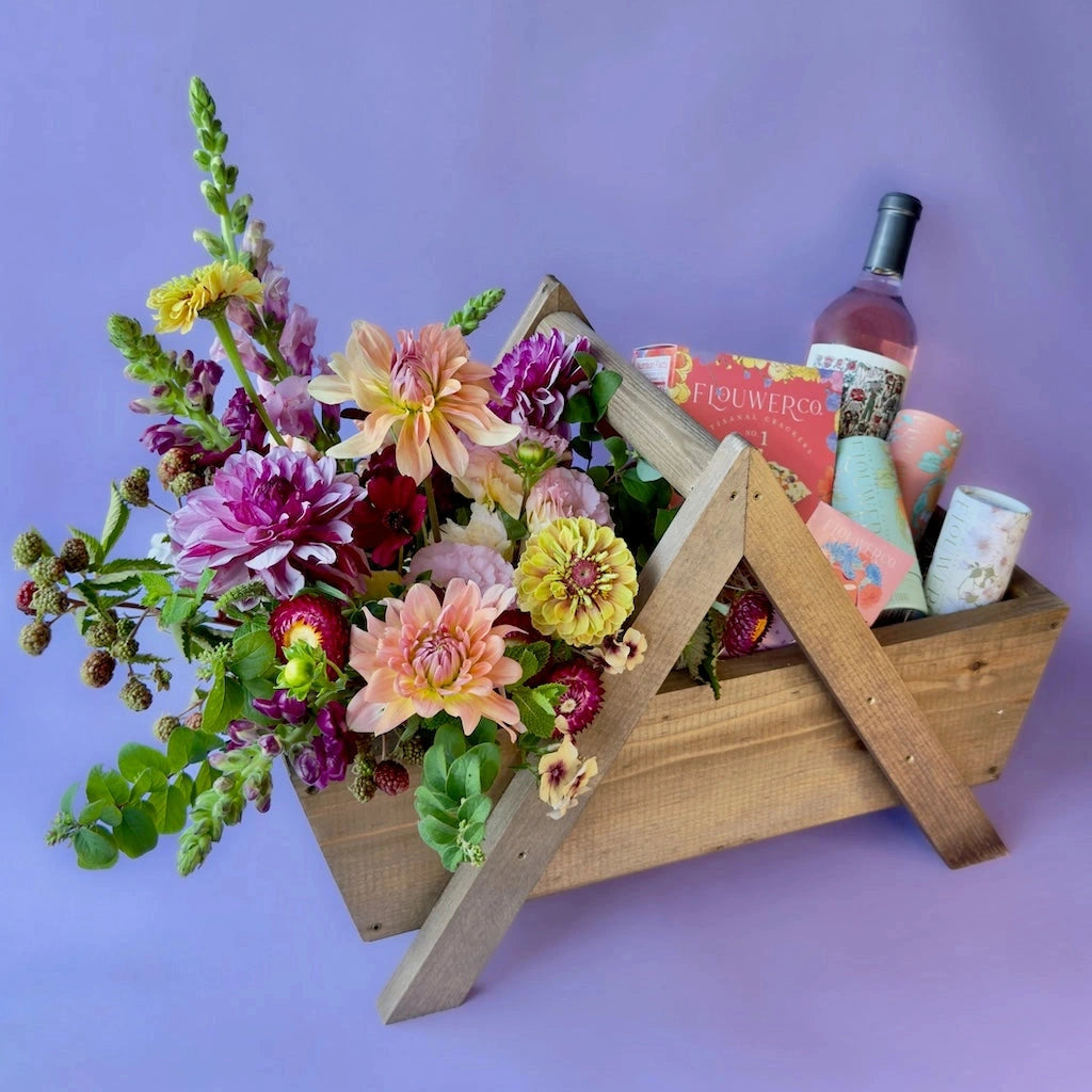 Wooden crate with flowers, a bottle of wine, and various gifts on a purple background