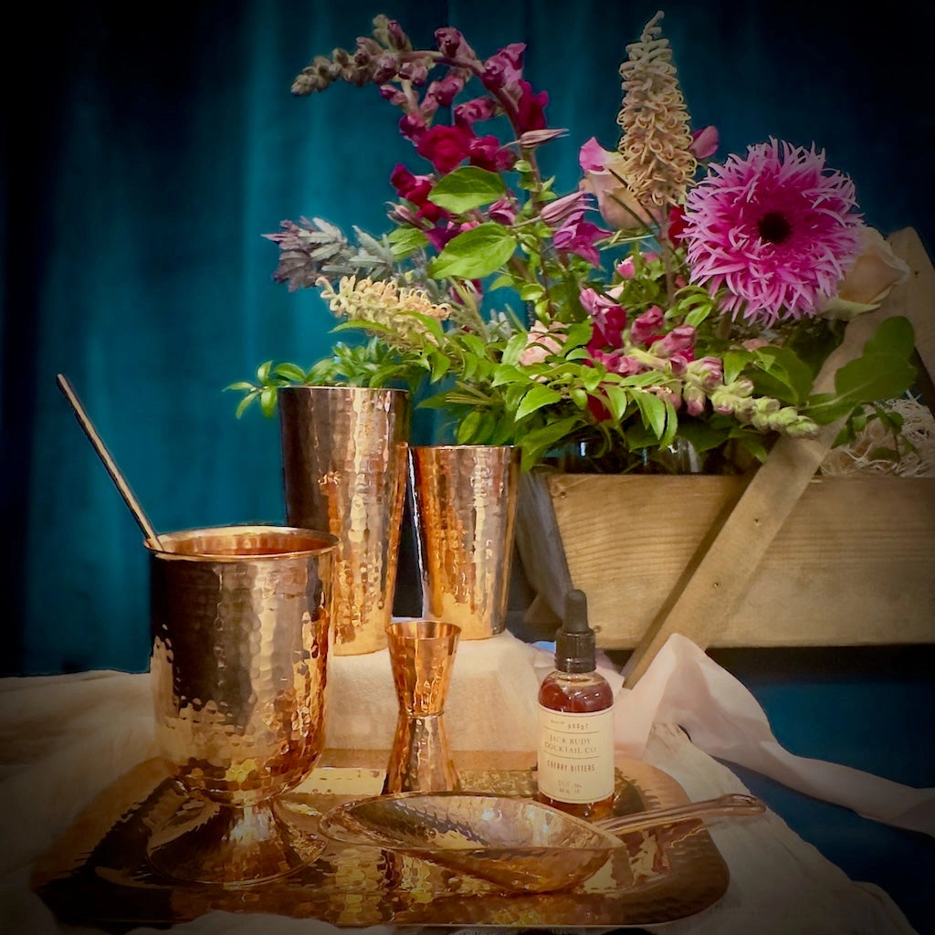 A unique handmade wooden gift basket filled with flowers, copper barware from Sertodo Copper, and Jack Rudy bitters.