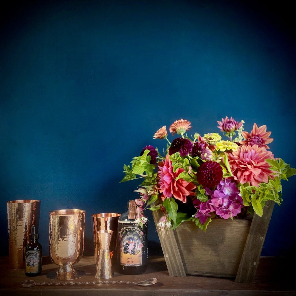 A gift basket featuring a sultry and sexy combo of handmade hammered copper barware, botanical syrups and bitters, and luscious blooms. 