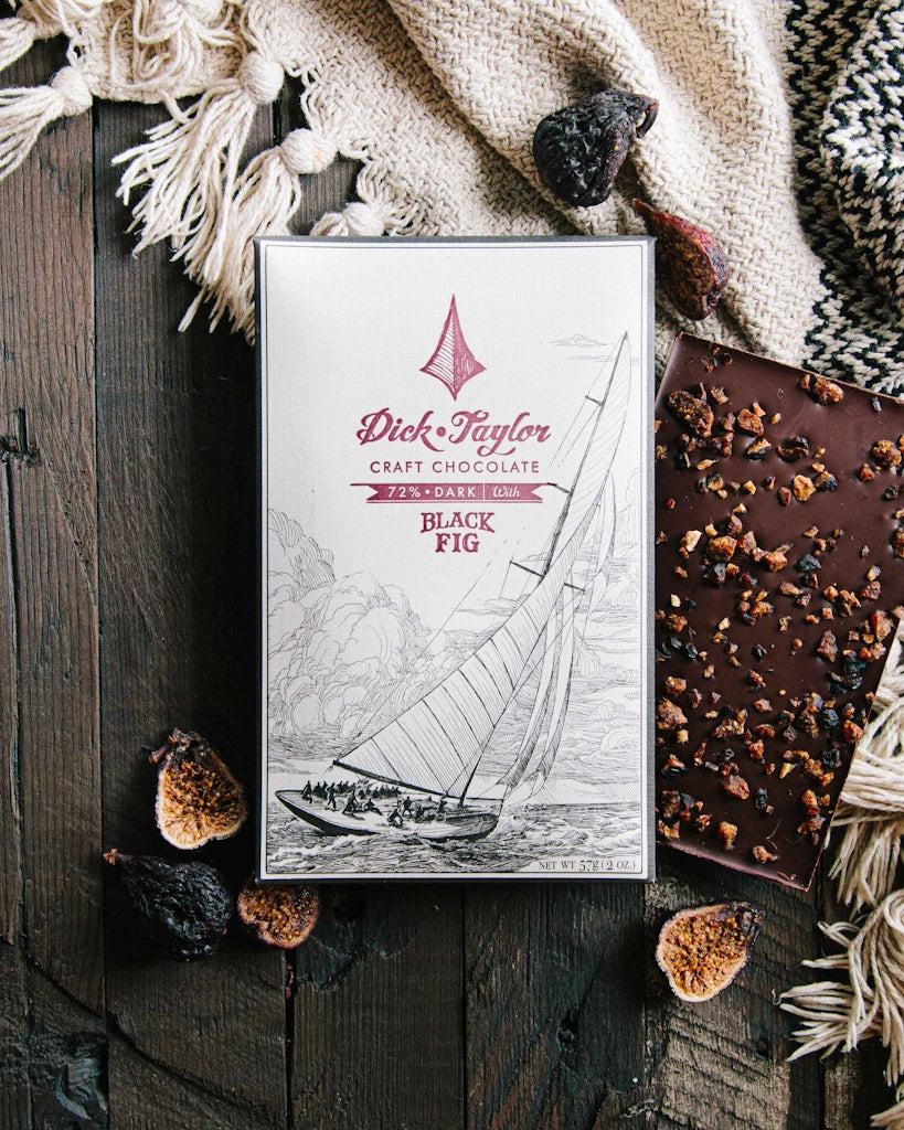 Dick Taylor craft chocolate bar with 'Black Fig' flavor on a wooden surface with decorative elements.