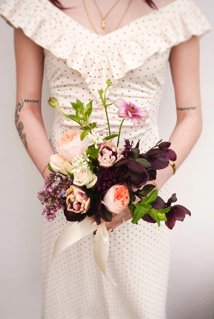 Person holding a bouquet of flowers wearing a white dress with ruffled shoulders.