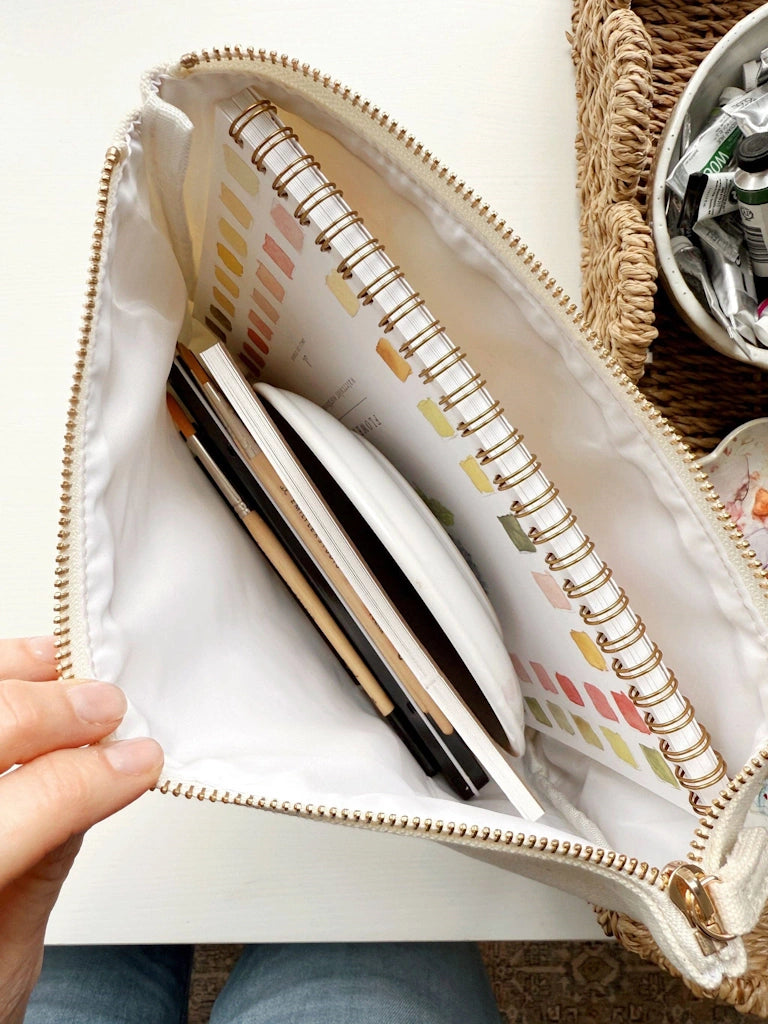 Open white pouch with spiral-bound notebook and pens on a light surface.