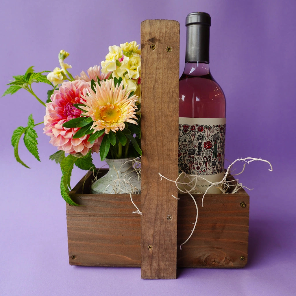 Wine bottle with floral arrangement in a wooden crate on a purple background