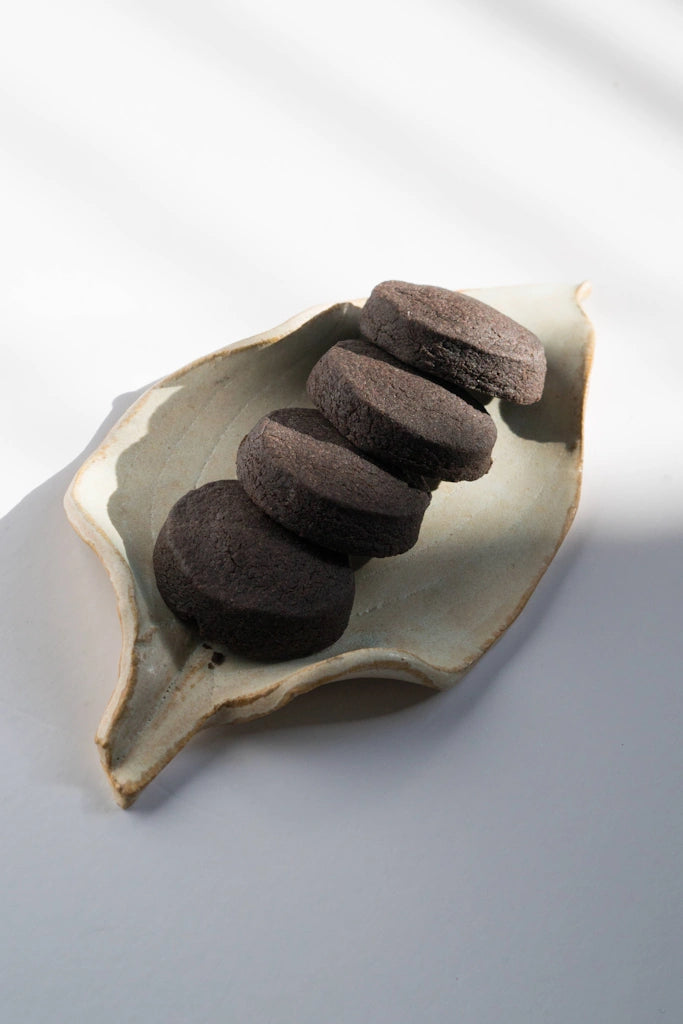Stack of dark brown shortbread cookies on a ceramic leaf-shaped dish against a light gray background