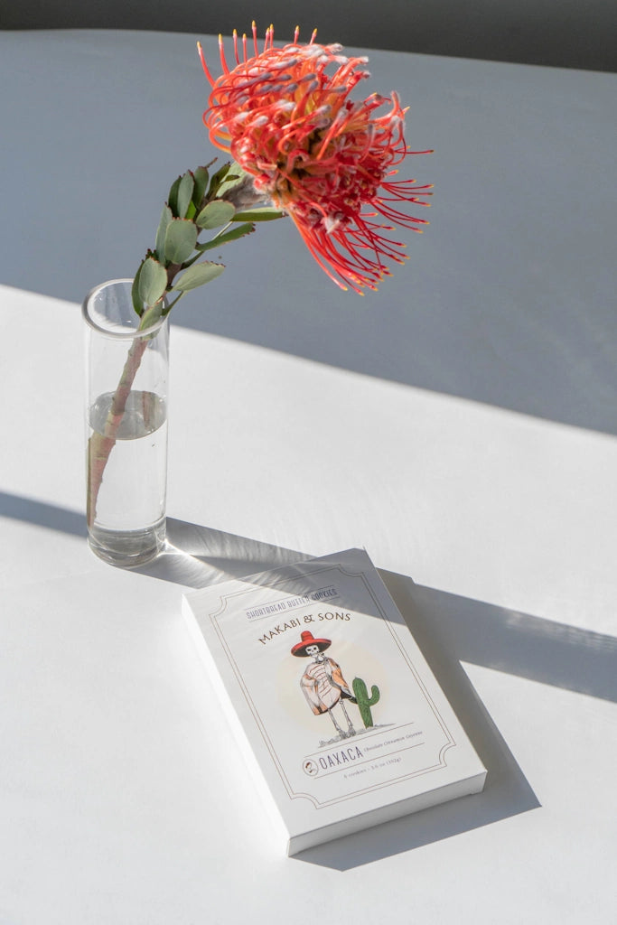 Box of shortbread cookies with a cactus illustration next to a vase with a red flower on a white surface