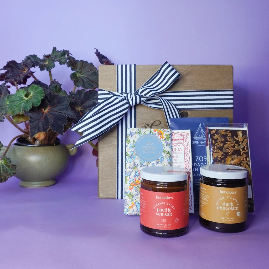 Gift box with a striped ribbon, two jars of caramel and chocolate and chocolate bars on a purple background