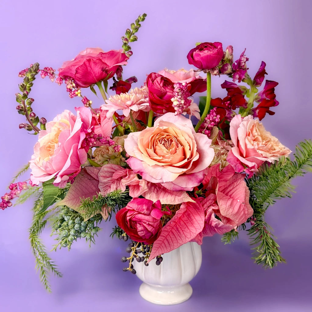 Bouquet of pink and red flowers in a white vase against a purple background