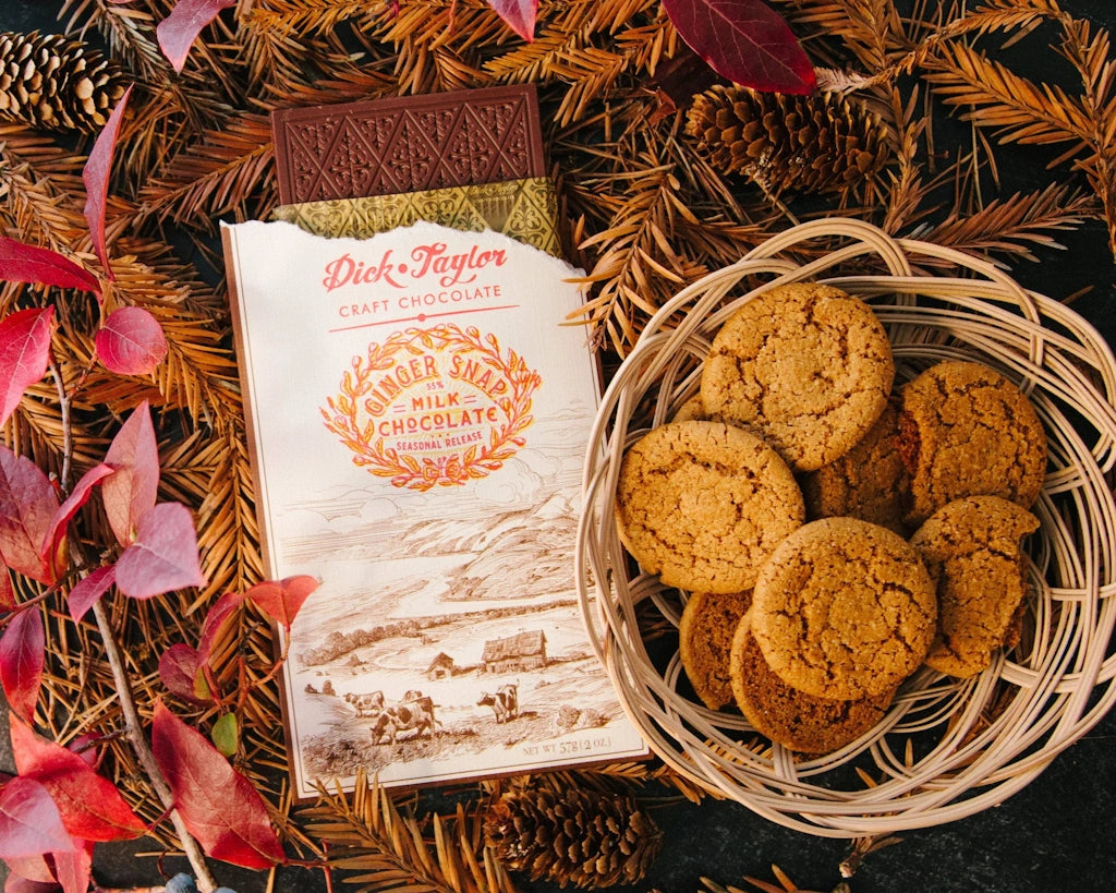 Basket of cookies next to a bar of Dick Taylor chocolate on a decorative background with leaves and pine cones.