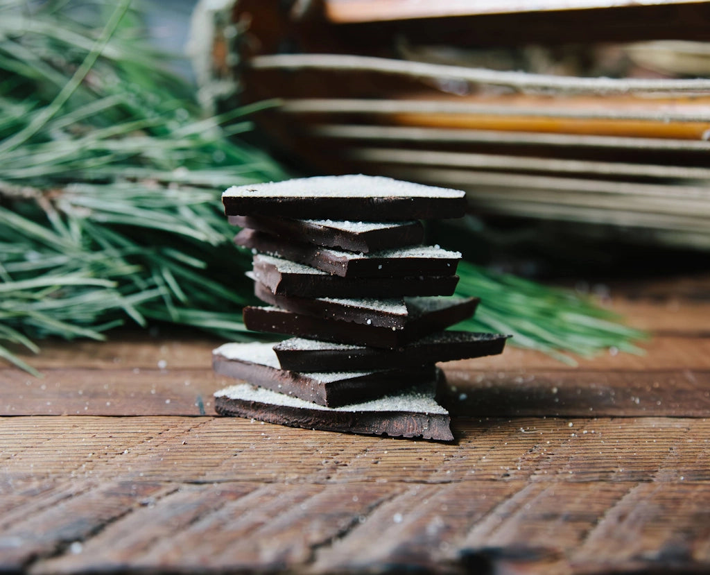 Stack of dark chocolate bars on a wooden surface with greenery in the background