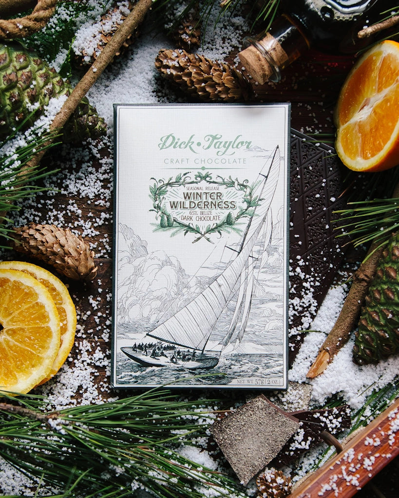 Chocolate bar packaging with sailboat illustration surrounded by oranges, pine cones, and snow-like sprinkles.