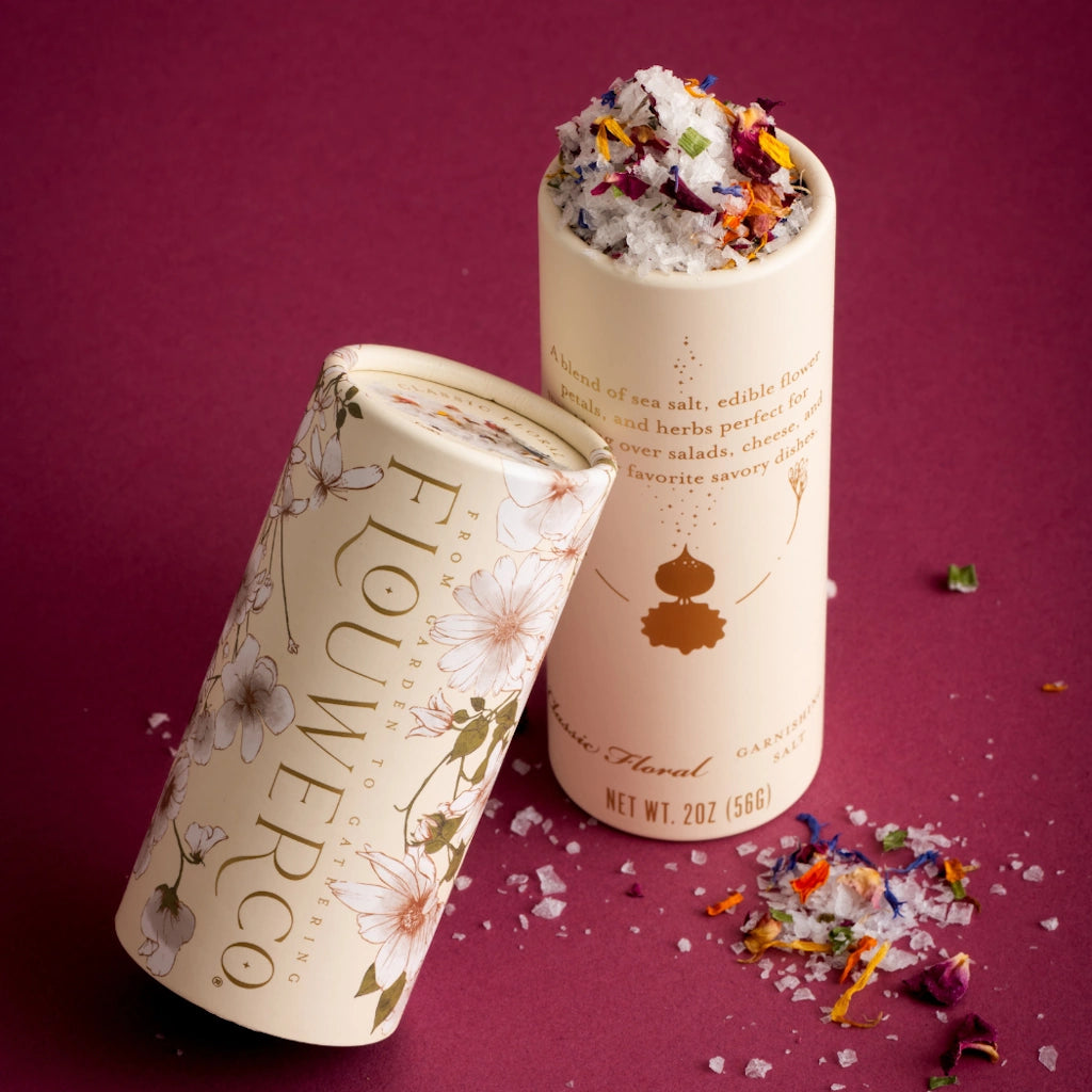 Two cylindrical containers of 'Flouwer Co.' flower salt on a purple background