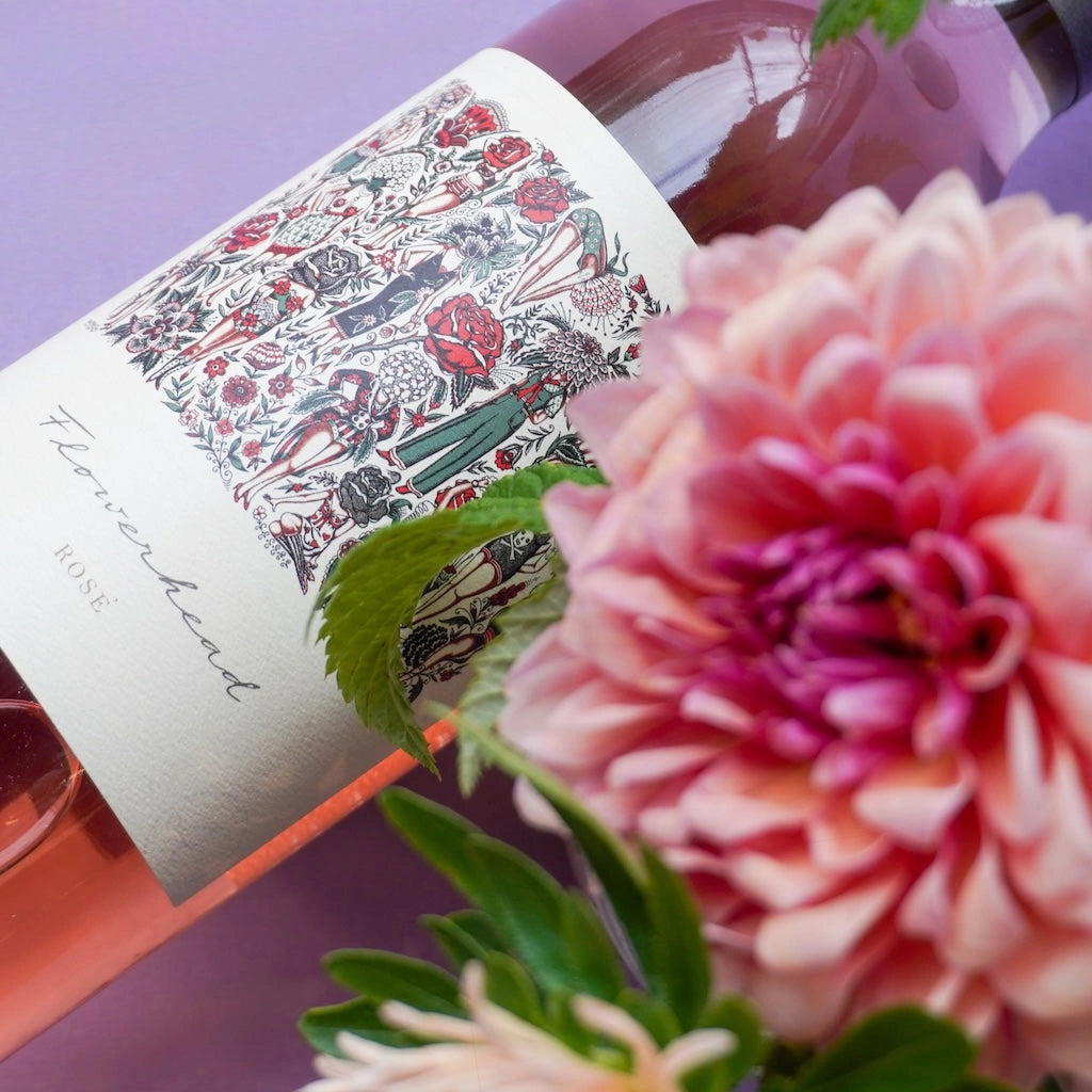 Wine bottle of Mark Ryan Flowerhead  Rose with decorative label and pink flowers on a purple background