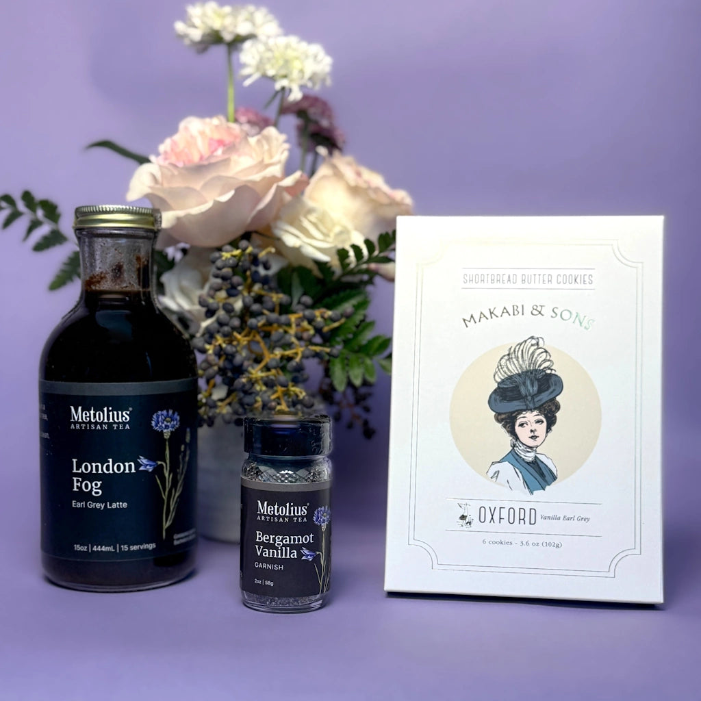 Two bottles of Metolius tea and a box of Makabi & Son cookies on a purple background with flowers.