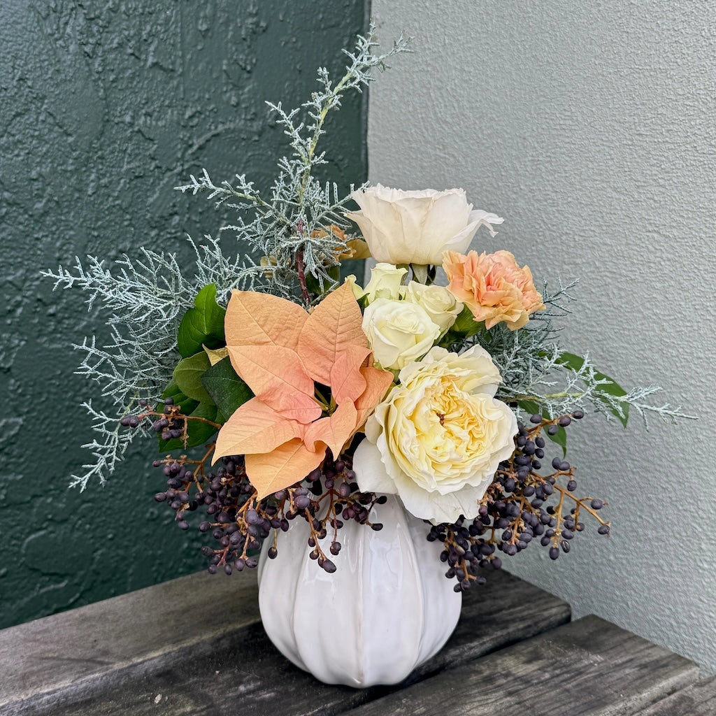 Floral arrangement in a white ceramic vase against a gray wall.