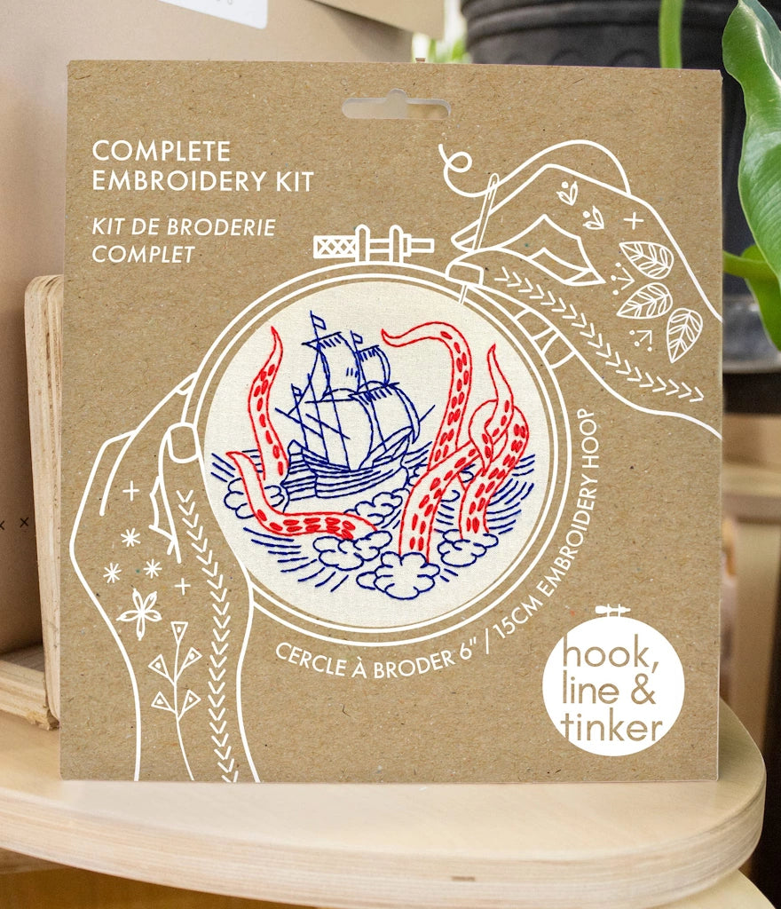 Complete embroidery kit packaging with ship design on a wooden surface