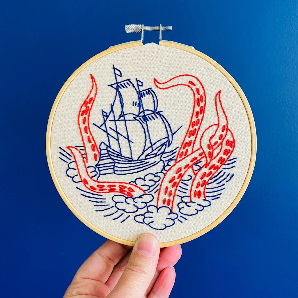 Embroidery hoop with a ship and tentacle design against a blue background