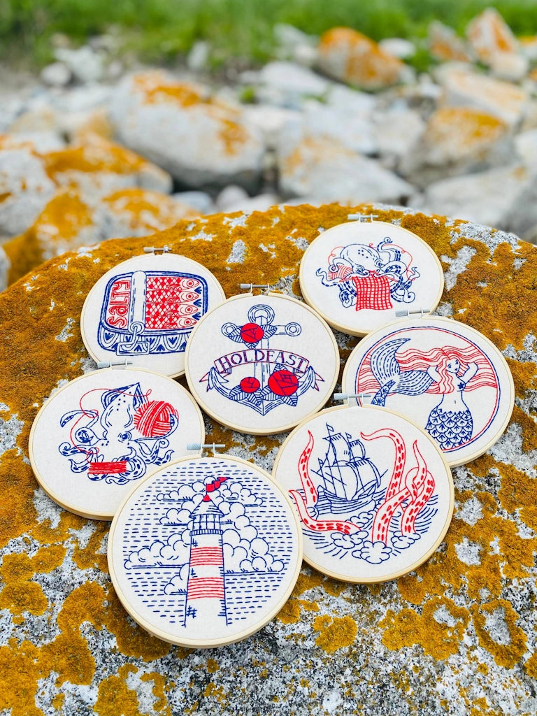 Decorative embroidery kit designs with red and blue designs on a lichen covered rock