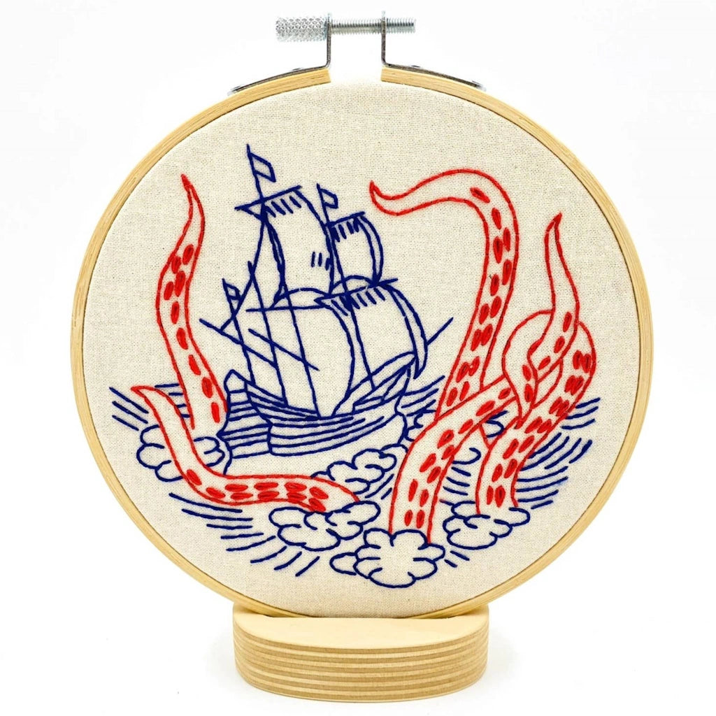 Embroidery hoop with a ship and tentacle design on white fabric.