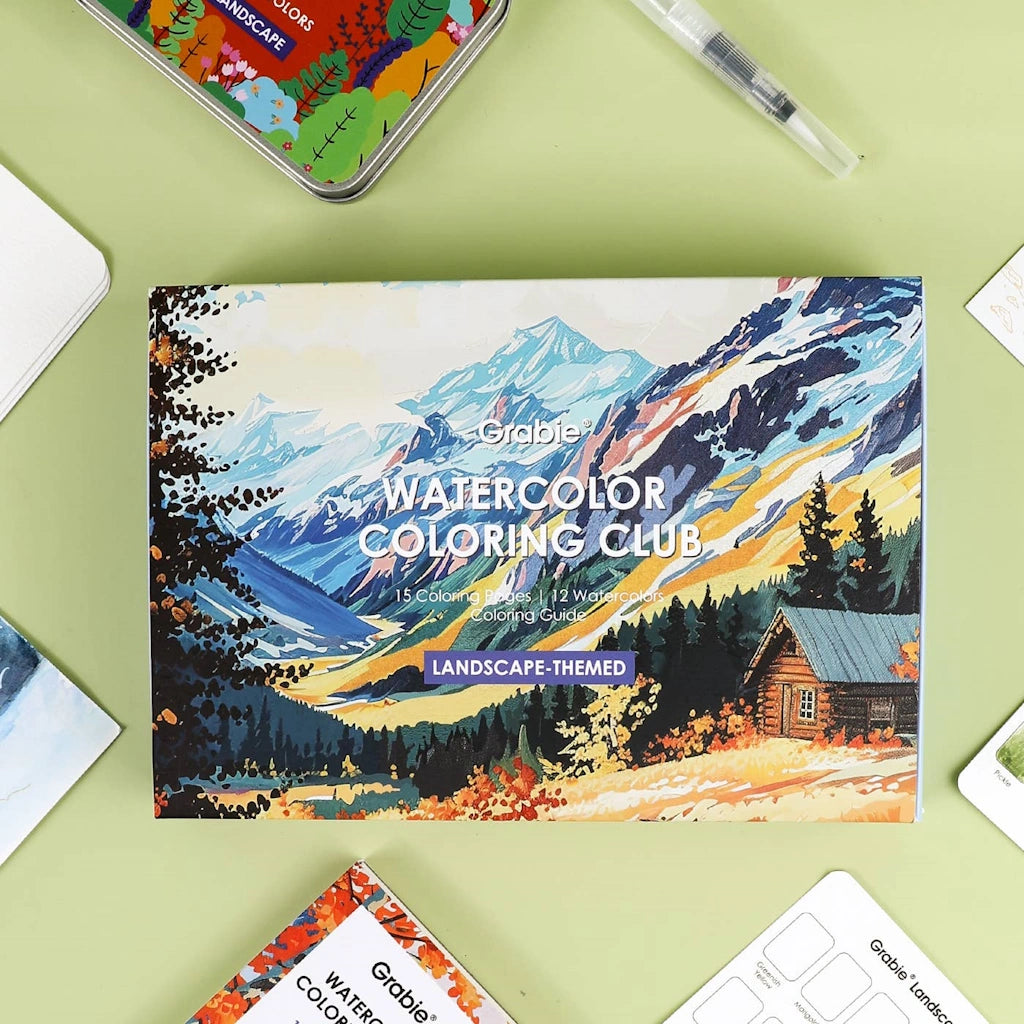Grable Watercolor Coloring Club landscape-themed coloring book on a green surface with a pen and phone.
