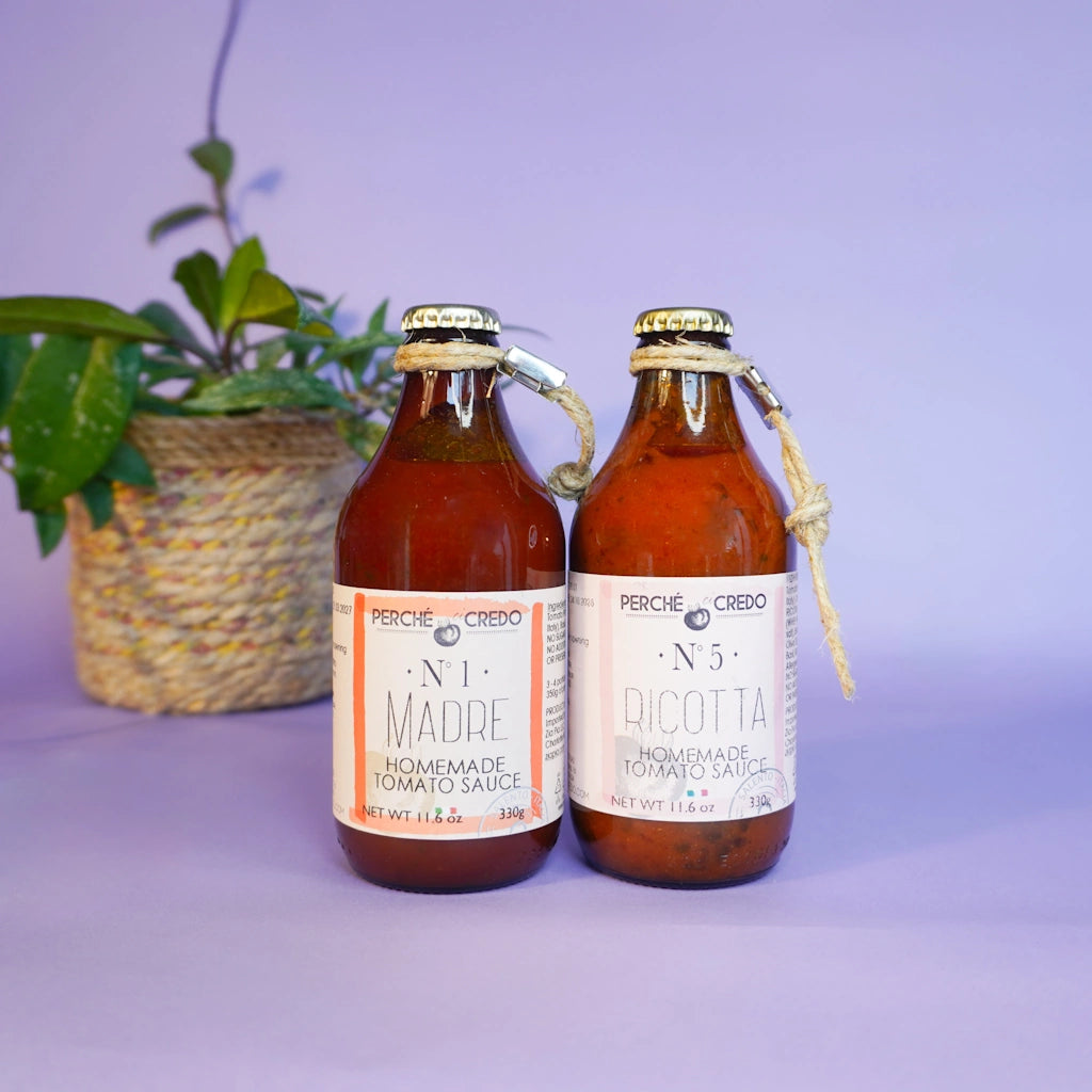Two bottles of Percheè Creéo tomato sauce on a purple background with a plant.