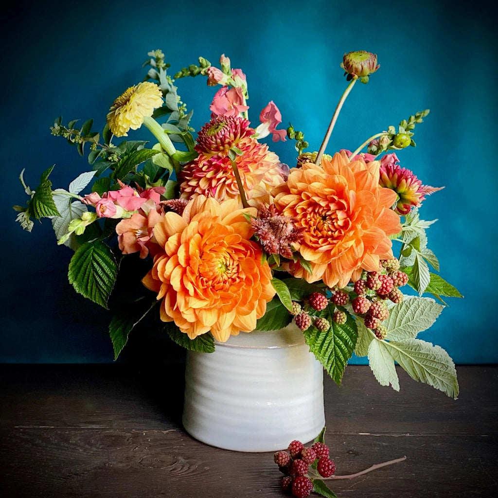 Campanula Design's "Mandarin" floral arrangement features a palette of soft pinks, buttery yellows, peach, and shades of orange designed in a ceramic vessel. 