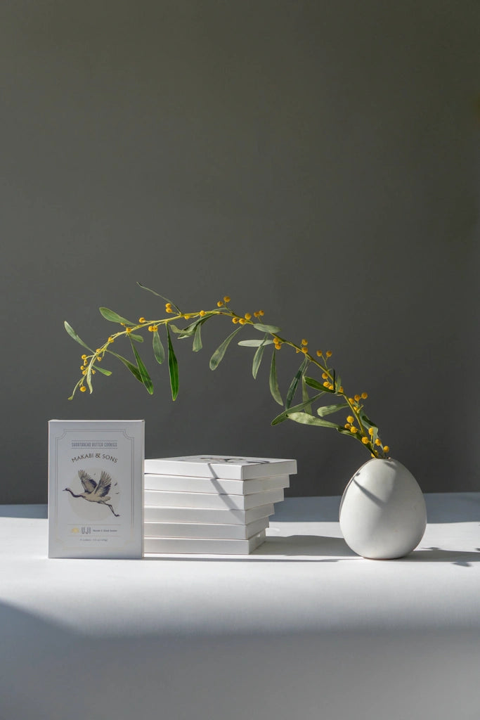 White vase with greenery on a stack of shortbread cookies against a gray background
