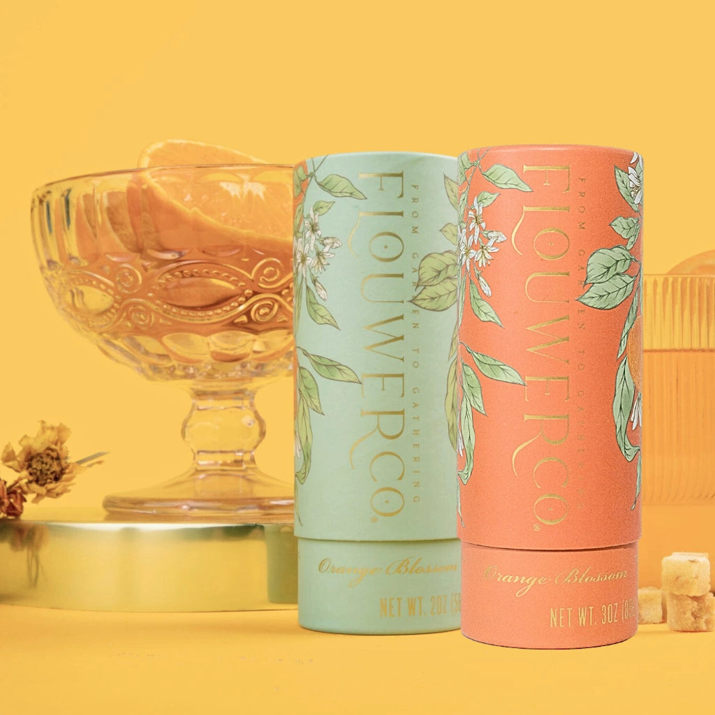Two cylindrical containers of orange  blossom cocktail cubes from Flouwer Co. with floral designs on a yellow background