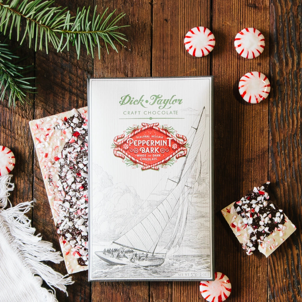 Box of Dick Taylor peppermint bark on a wooden surface with candy canes and Christmas decorations.