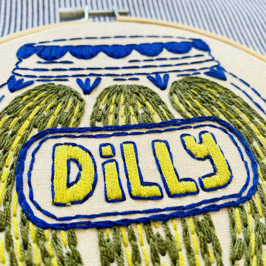 Embroidery hoop with 'Dilly' text and cactus design on a striped fabric background