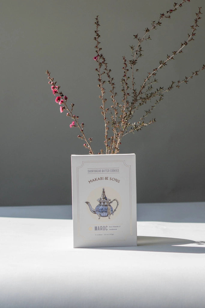 Package of rose pistachio cardamom shortbread cookies with a teapot illustration on a gray background with dried branches.