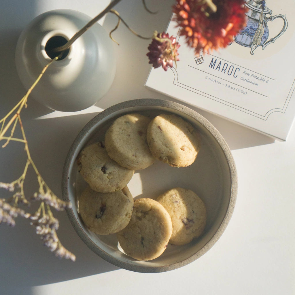 Bowl of cookies with a decorative box labeled 'Maroc' and a vase in the background.