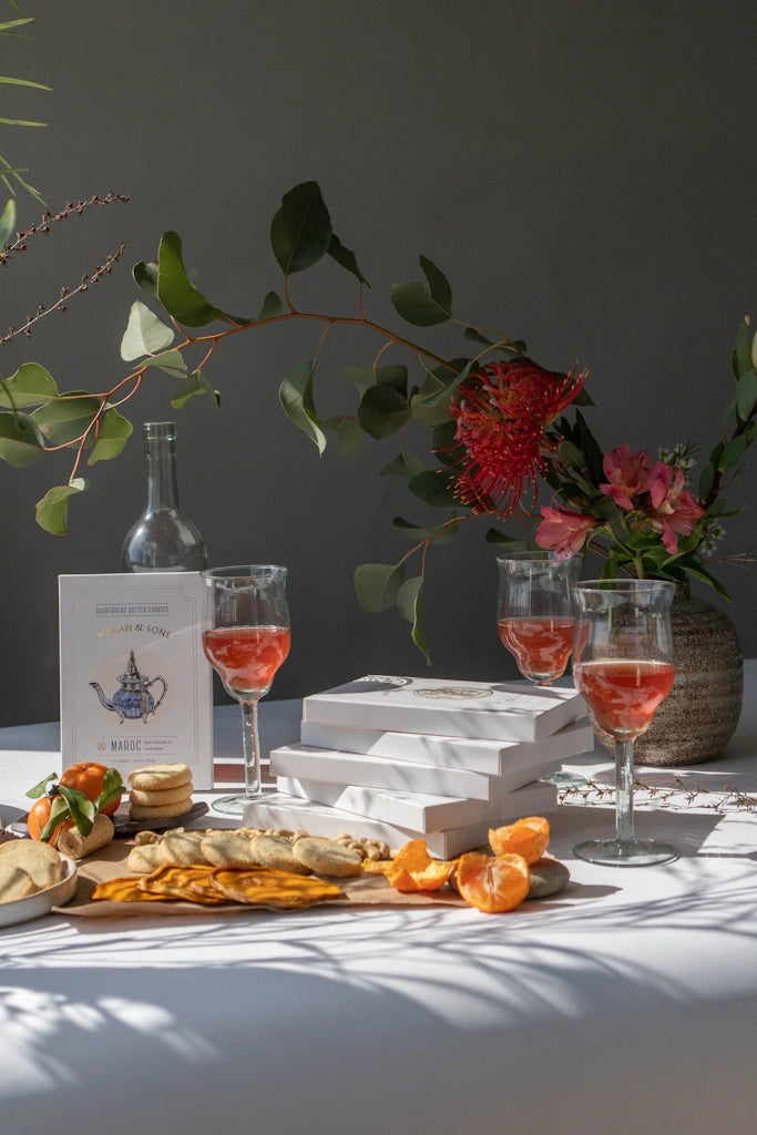 Table setting with wine glasses, snacks, shortbread cookie boxes and a vase of flowers on a gray background