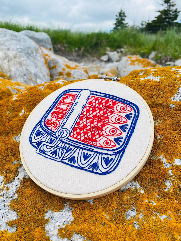 Embroidery hoop with a red and blue design on a lichen-covered rock
