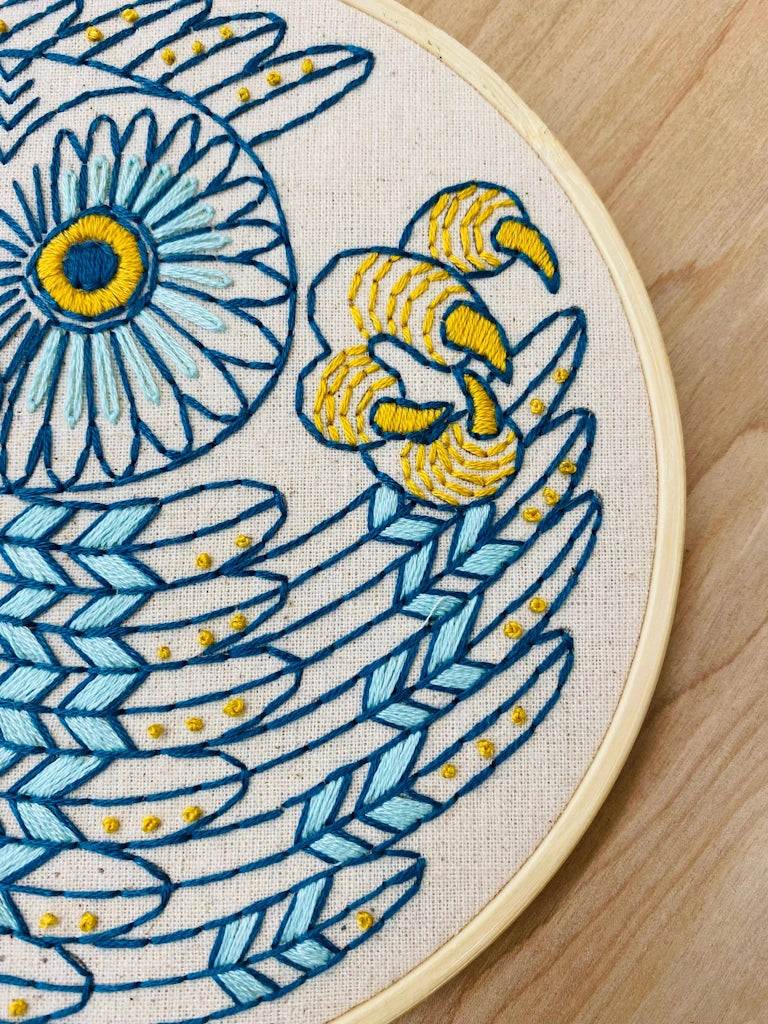 Embroidery hoop with blue and yellow owl design on a wooden surface