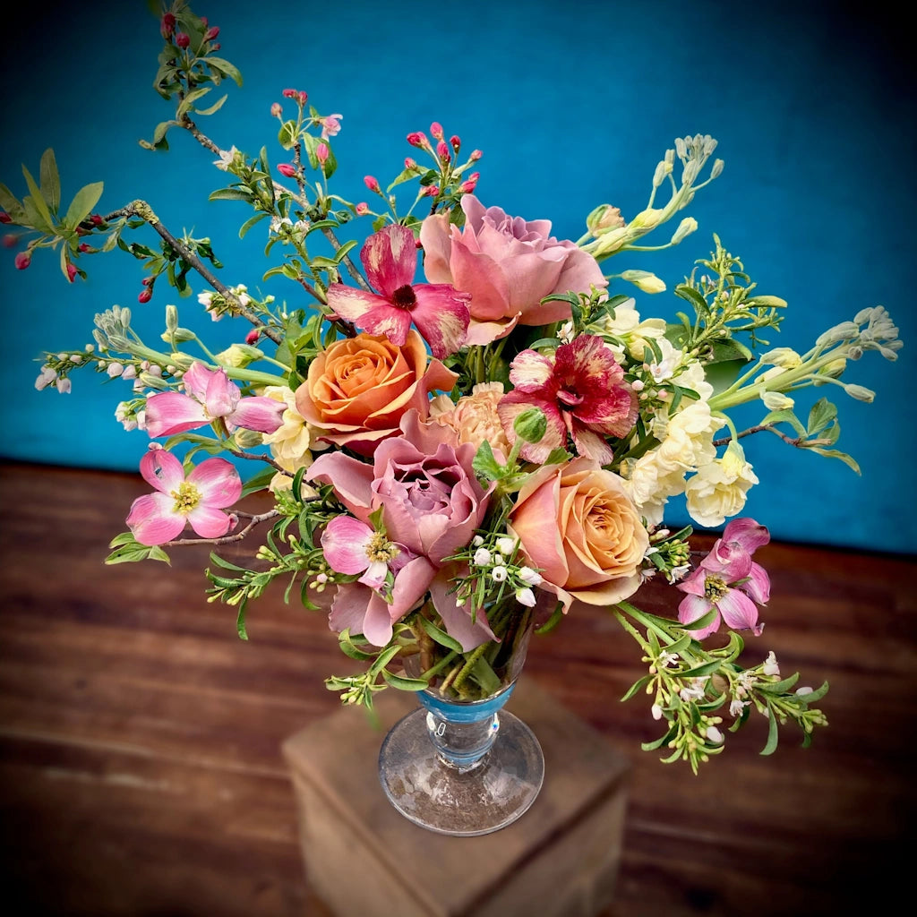 Campanula Design Studio's "Sugar Mama" floral arrangement features a seasonal palette of muted pinks, warm peaches, and cream tones designed in a simple clear pedestal vase.
