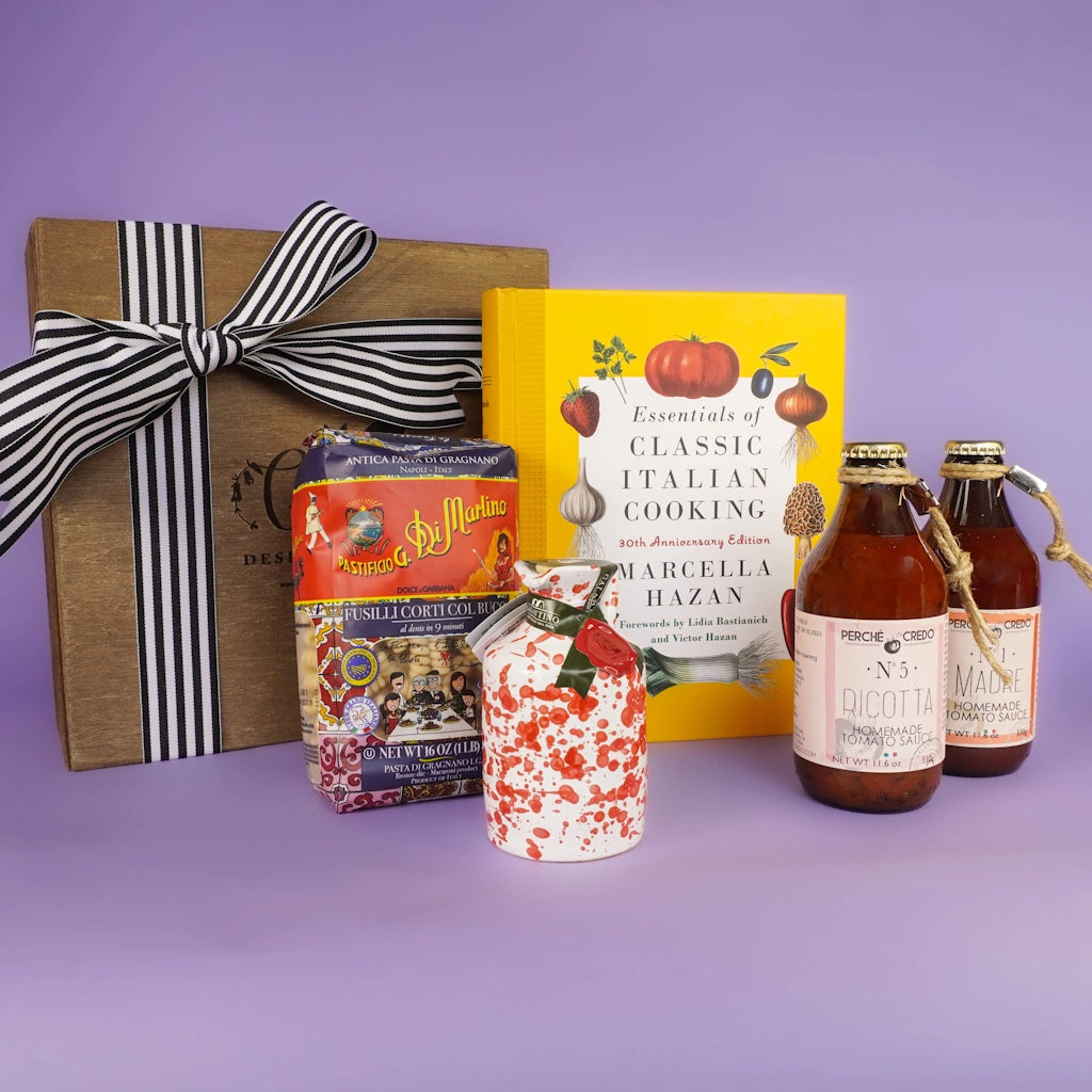 Gift box with a ribbon, cookbooks, and Italian themed goods on a purple background.  Available for sale from Campanula Design Studio, Seattle florist and gift basket company in the Magnolia neighborhood.