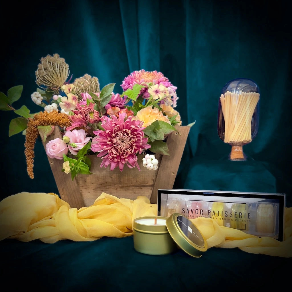 A gift basket comprised of a candle, a Skeem match cloche, macarons, and flowers.