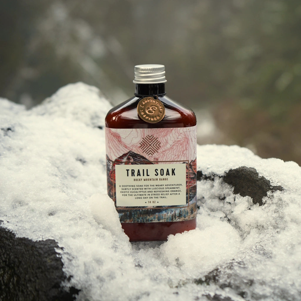 Bottle of 'Trail Soak' on a snowy rock with a mountainous background