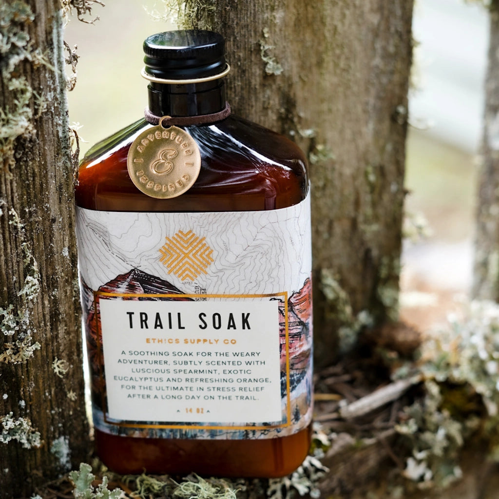 Bottle of 'Trail Soak' against a natural background with trees and foliage.