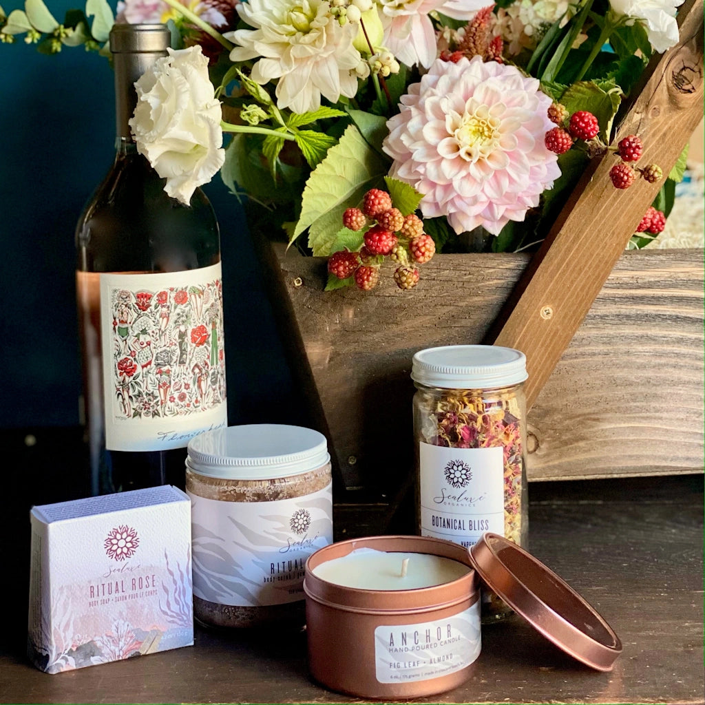 Campanula Design Studio's Tranqulity gift basket features a soft floral, Ritual rose soap, Ritual rose body scrub (rose body butter, bath tea, or bath salt may be substituted if unavailable), Botanical Bliss Steam Facial (bath tea, salt, or soap may be substituted),Sealuxe tin candle (scent varies), and a  bottle of TÖST non-alcoholic sparkling beverage (or upgrade to a bottle of wine if you prefer)