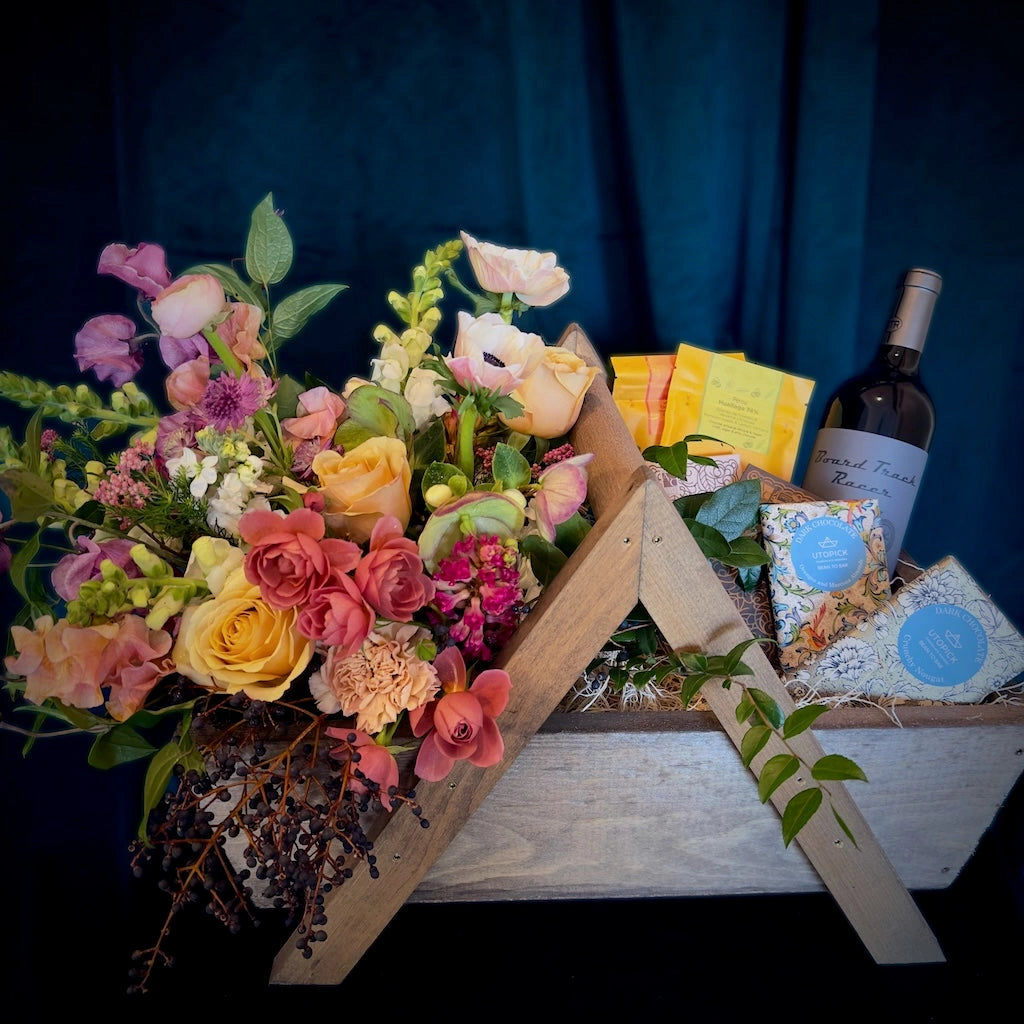 A handmade wooden gift basket featuring a seasonally inspired floral, bars of fine chocolate, and a bottle of Mark Winery Wines wine