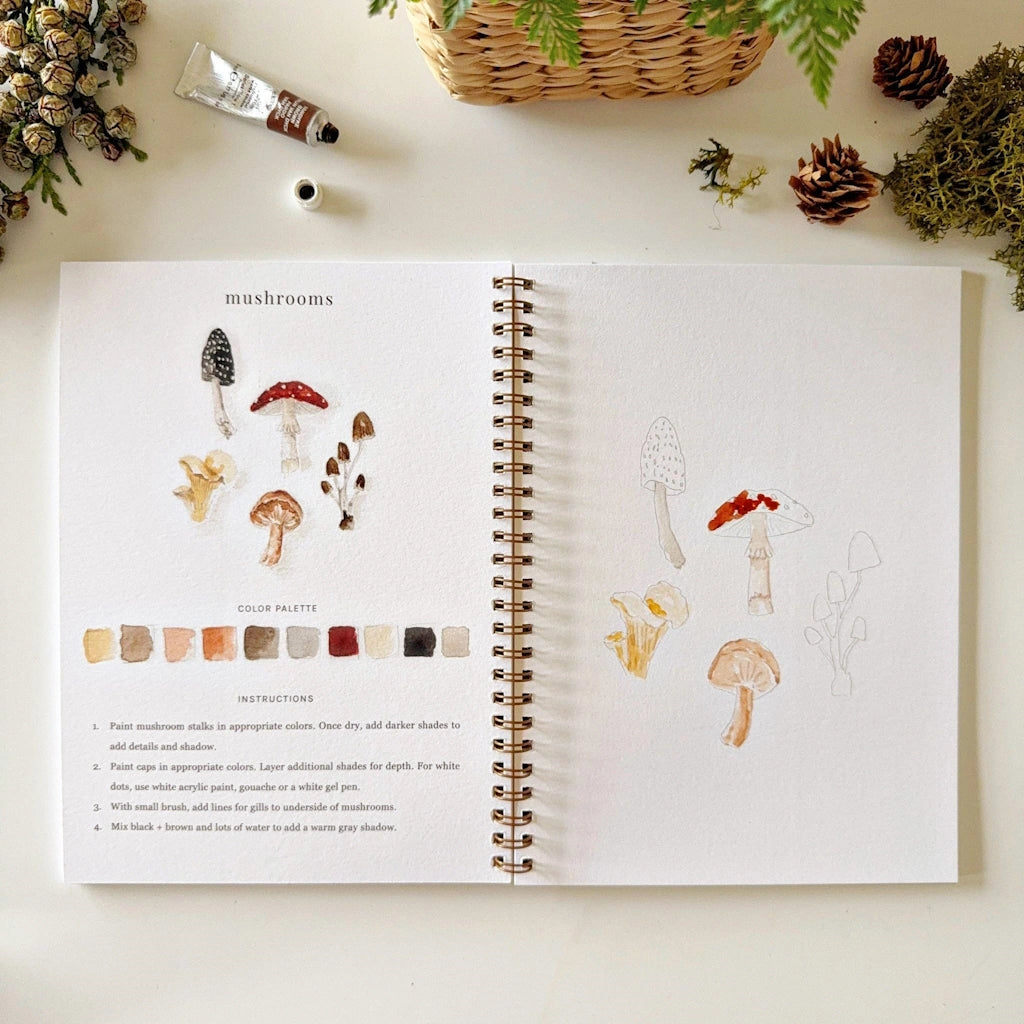 Open book with illustrations of mushrooms and color swatches on a white surface with decorative items.
