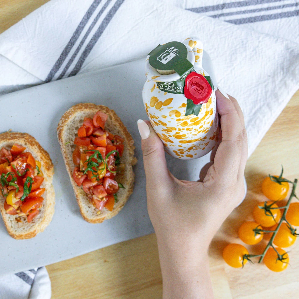 Hand holding a bottle of olive oil with bread and tomatoes on a table