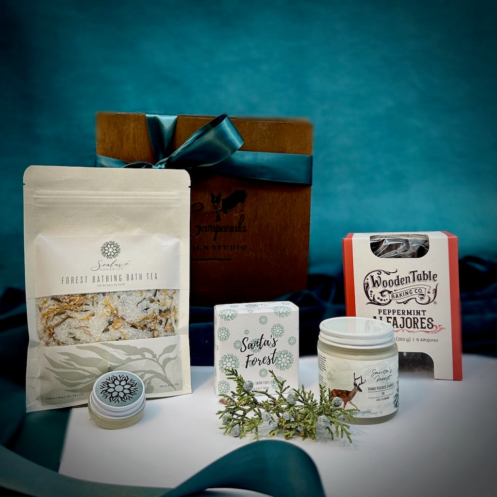 A curated gift box of Sealuxe spa products: forest bath tea, a candle, a soap, a mint lip balm and some delicious Wooden Table Baking Co. dark chocolate peppermint alfajores artfully designed in a handmade wooden gift box. By Seattle gift basket company Campanula Design Studio.